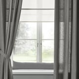 Grey LJUNGSNÄRJA cushion on windowsill with matching curtains, soft light.