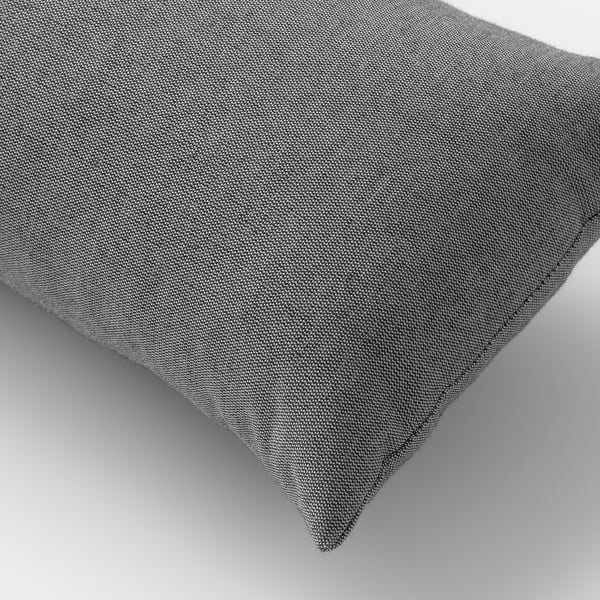 Close-up of a soft, grey, recycled fabric cushion, resting on a plain surface, showcasing its plush texture and fine stitching.