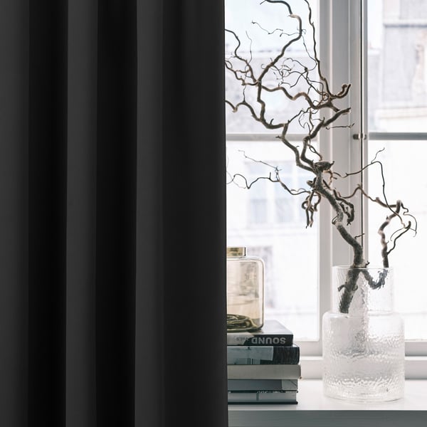 Modern room decor: MAJGULL blackout curtains frame a window with a textured vase holding dried branches and stacks of books.