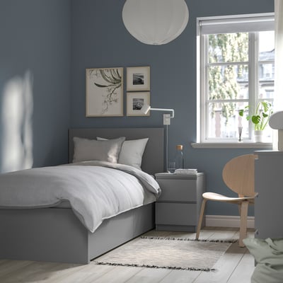 Modern bedroom with MALM bed, white linens, wooden chair, grey bedside table, large window, blue walls, and wall art.
