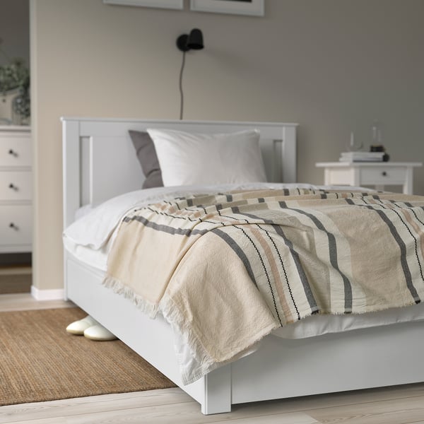 Minimalist bedroom with white MANTELFLY bed, light grey striped throw, two pillows, grey accent, white dresser, wooden floor, small rug.