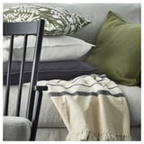 Grey and white striped MANTELFLY throw blanket with fringe, draped over a couch, paired with green and white cushions.