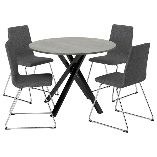 Modern round dining table with sleek metal legs and three matching grey fabric chairs.