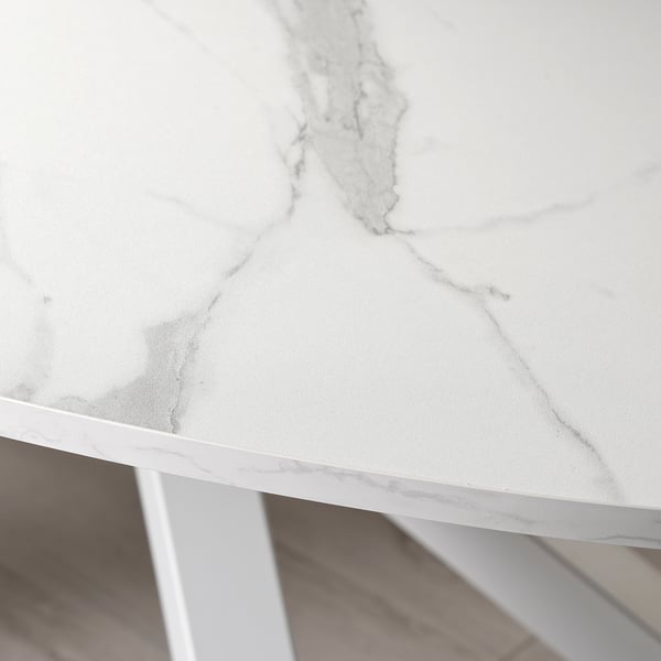 A modern, white, oval tabletop with sleek edges, supported by metal legs. Veins are visible across the surface, adding texture and elegance.