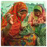 Two women sewing in colorful traditional attire.