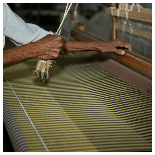 Hands weaving green and navy striped fabric on a loom.