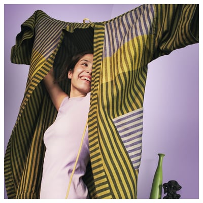 Woman in striped yellow-green bathrobe smiling, holding cloth over head.