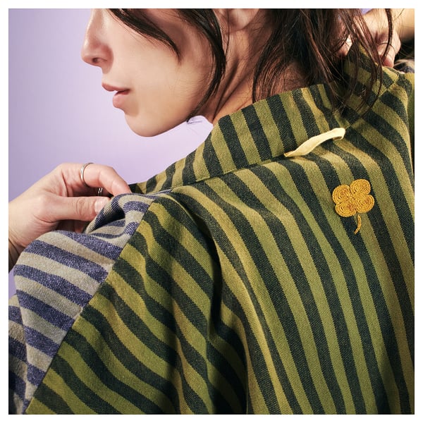 Person wearing green striped MÄVINN bathrobe with yellow clover emblem, adjusting collar.