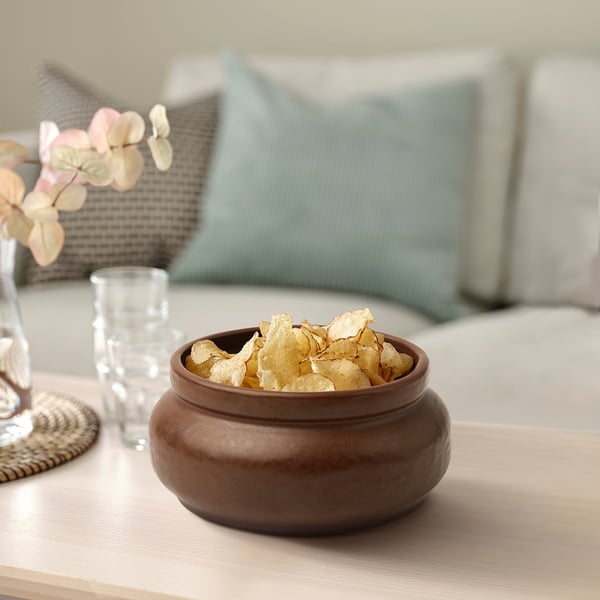 Brown ceramic bowl with chips on table, glass, and decor, handmade and functional.