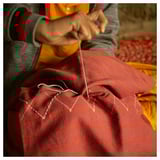 Person sewing red striped fabric. Yellow clothing visible. Thread and needle in use.