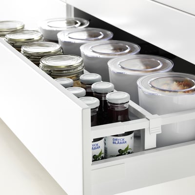 White drawer organizer fully extended, holding jars, containers, and a box, showcasing accessible storage.