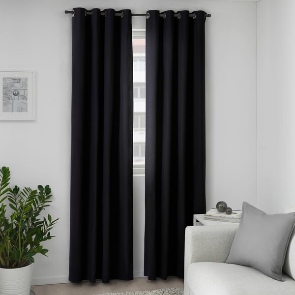 Black curtains with eyelets hang by a window, blocking light and providing privacy. A large plant and light gray sofa are nearby.