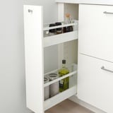 White kitchen cabinet with pull-out drawer, holding spice jars and olive oil bottle.
