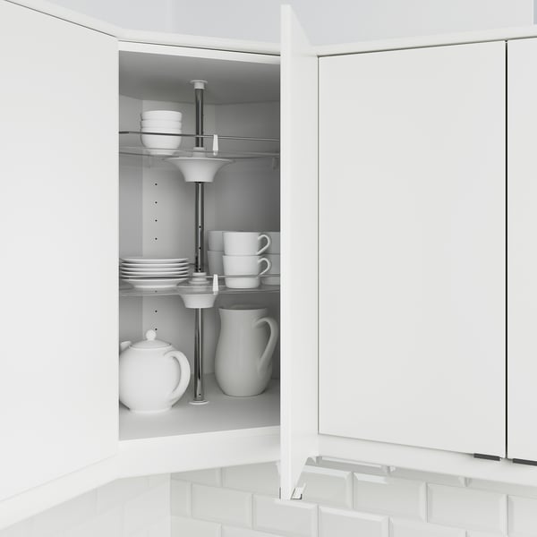Open white corner kitchen cabinet showing adjustable shelves holding stacks of white plates, cups, and a teapot.