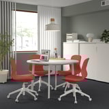 Meetings area with round MITTZON table, red chairs, white cabinet, green wall & large window.