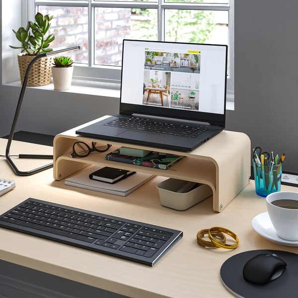 Organized workspace with laptop on stand, keyboard, mouse, lamp, plants, and coffee.