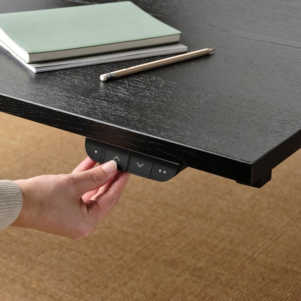 Hand pressing button on black desk control panel with books and pen on the desk.