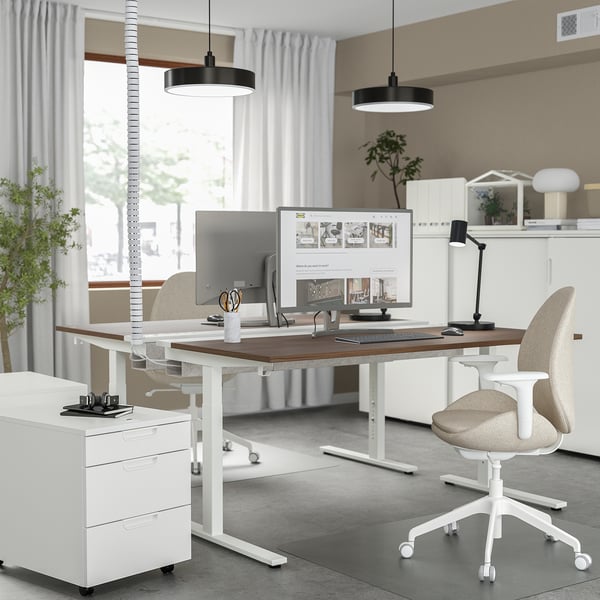 Modern home office with MITTZON desk, white, wooden top, adjustable height, two beige chairs, dual monitors, and ambient lighting.