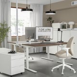 Modern home office with MITTZON desk, white, wooden top, adjustable height, two beige chairs, dual monitors, and ambient lighting.