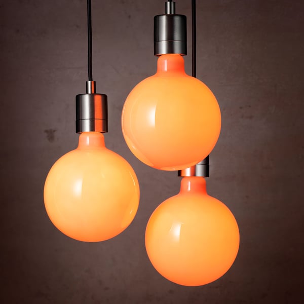 Three round, orange light bulbs hang from black cables against a dark wall. Each bulb has a warm, candle-like glow and emits a cozy light.