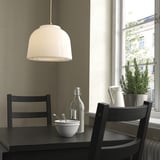 Minimalist kitchen nook with black furniture, white MUDDERVERK pendant lamp, dark table, two chairs, plant, and bowl of spoons.