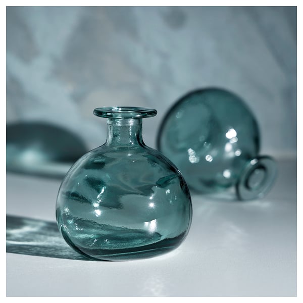 A teal-colored MYRMOSAIK glass vase with a rounded, handcrafted design, showcased against a light background.