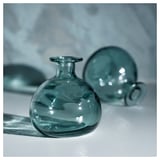 A teal-colored MYRMOSAIK glass vase with a rounded, handcrafted design, showcased against a light background.