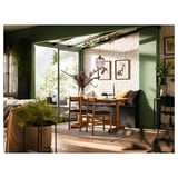 A cozy dining area with a wooden NACKANÄS table and chairs in a bright room with green walls and white brick.