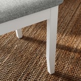 Modern dining chair with thick cushion, white frame, on woven rug.