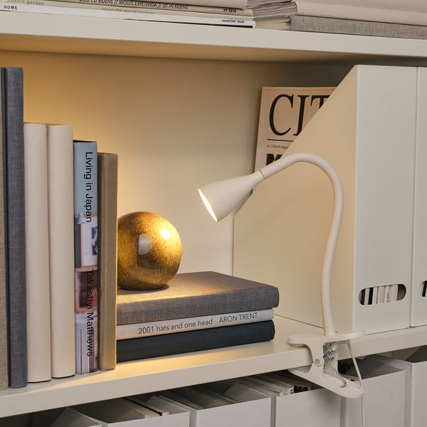Shelf with books & magazine, illuminated by a white, adjustable clamp lamp. A small globe decor rests atop books.