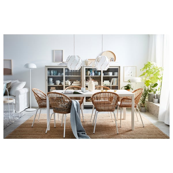 Chic dining area with wicker NILSOVE chairs, white table, and glass-fronted cabinet, adorned with plants and stylish decor.