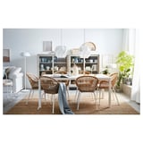 Chic dining area with wicker NILSOVE chairs, white table, and glass-fronted cabinet, adorned with plants and stylish decor.