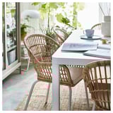 Gray wicker chair with bamboo, books, plates, and blue mug near window with plants.