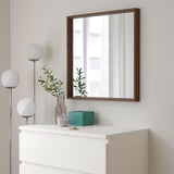 NISSEDAL mirror over white chest, reflecting window, with lamp, vase, and turquoise box.