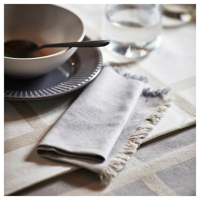 NISSÖGA napkins in cotton-jute, neutral tones, frayed edges, beside plate and glass.