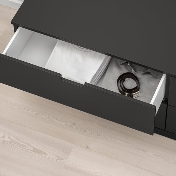 Black NORDLI drawer open, showing belt, soft-close mechanism visible, on light wood floor.