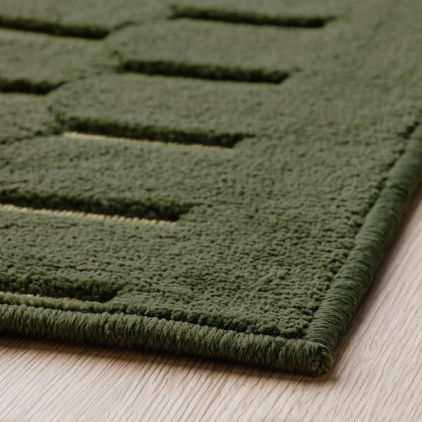 Green patterned rug, textured surface on wooden floor.