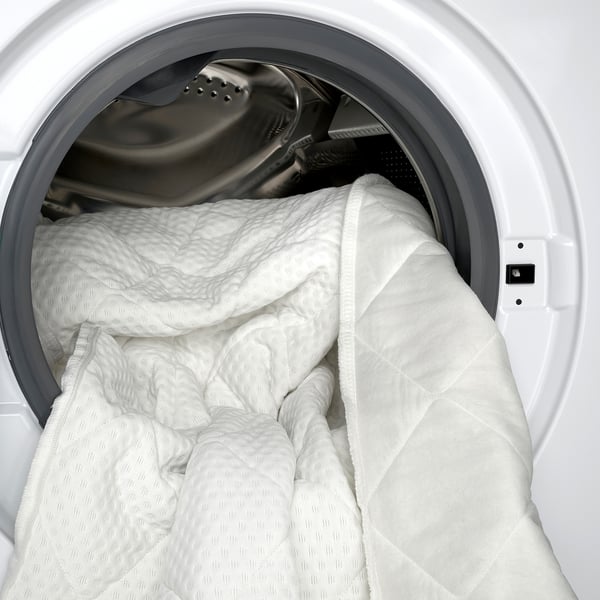 Washing machine with white bedding, showcasing easy cleanup of natural latex mattress pad with removable, machine-washable cover.