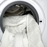 Washing machine with white bedding, showcasing easy cleanup of natural latex mattress pad with removable, machine-washable cover.
