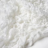 Soft white ruffled fabric, close-up view. Texture appears smooth and delicate, likely made from recycled polyester and acrylic.