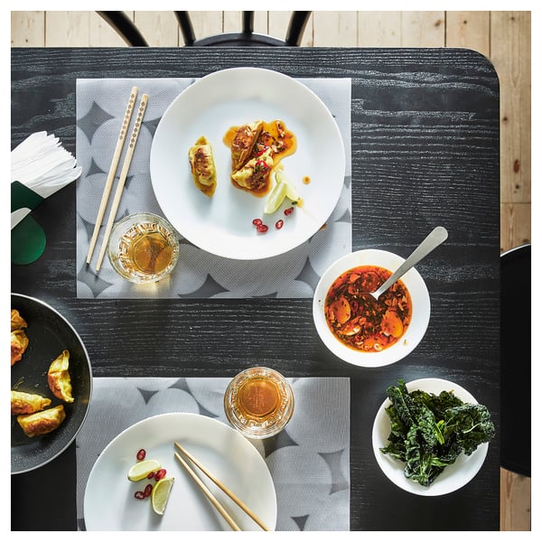 Dinner setup with white plates and bowls, chopsticks, colorful food on dark wooden table.