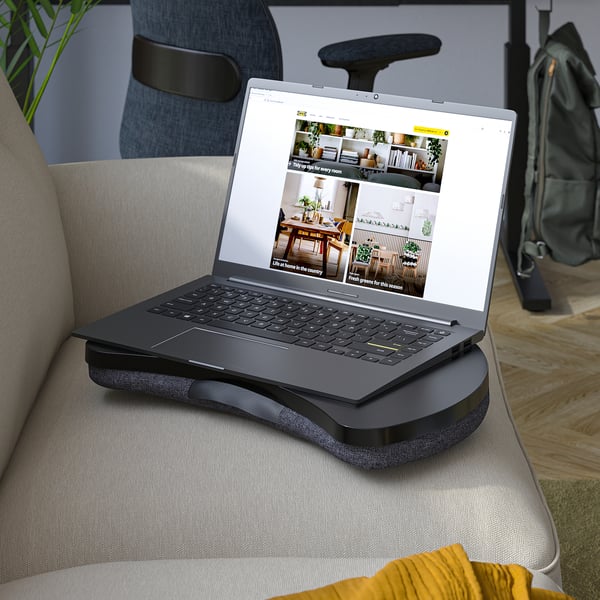 Laptop on gray cushion tray, used on light gray sofa. Display shows home decor tips.