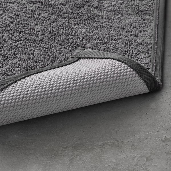 Textured grey bath mat with dark grey edge trim, showcasing its soft, machine-washable material.