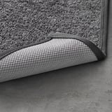 Textured grey bath mat with dark grey edge trim, showcasing its soft, machine-washable material.