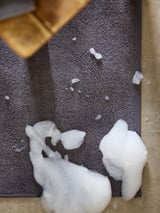 A grey bathroom mat with white soap suds on it. The mat is slightly crumpled and appears soft.