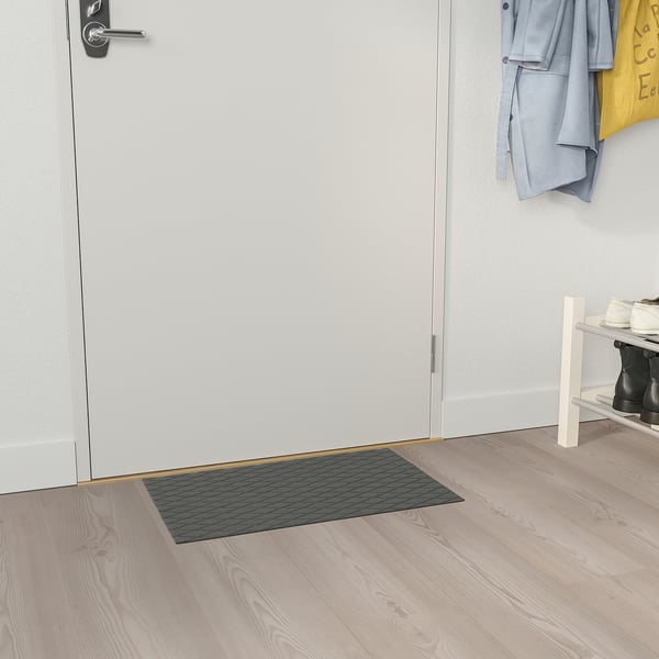 Grey ÖSTERILD recycled polyester doormat with diamond pattern under white door, right of wooden shoe rack.