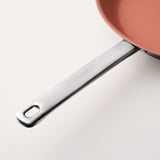 Modern stainless steel handle of pink ceramic frying pan, sleek design and durable quality.