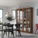 Modern dining room with OXBERG bookcase, white dishes, black chairs, striped rug, and large pendant lamp.