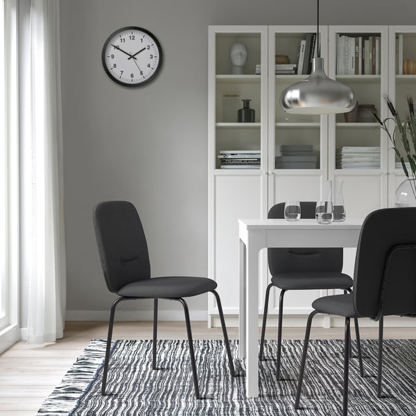 Modern dining area with white table, 3 black PÅBODA chairs, clock, bookshelf, rug, and pendant light.