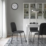 Modern dining area with white table, 3 black PÅBODA chairs, clock, bookshelf, rug, and pendant light.